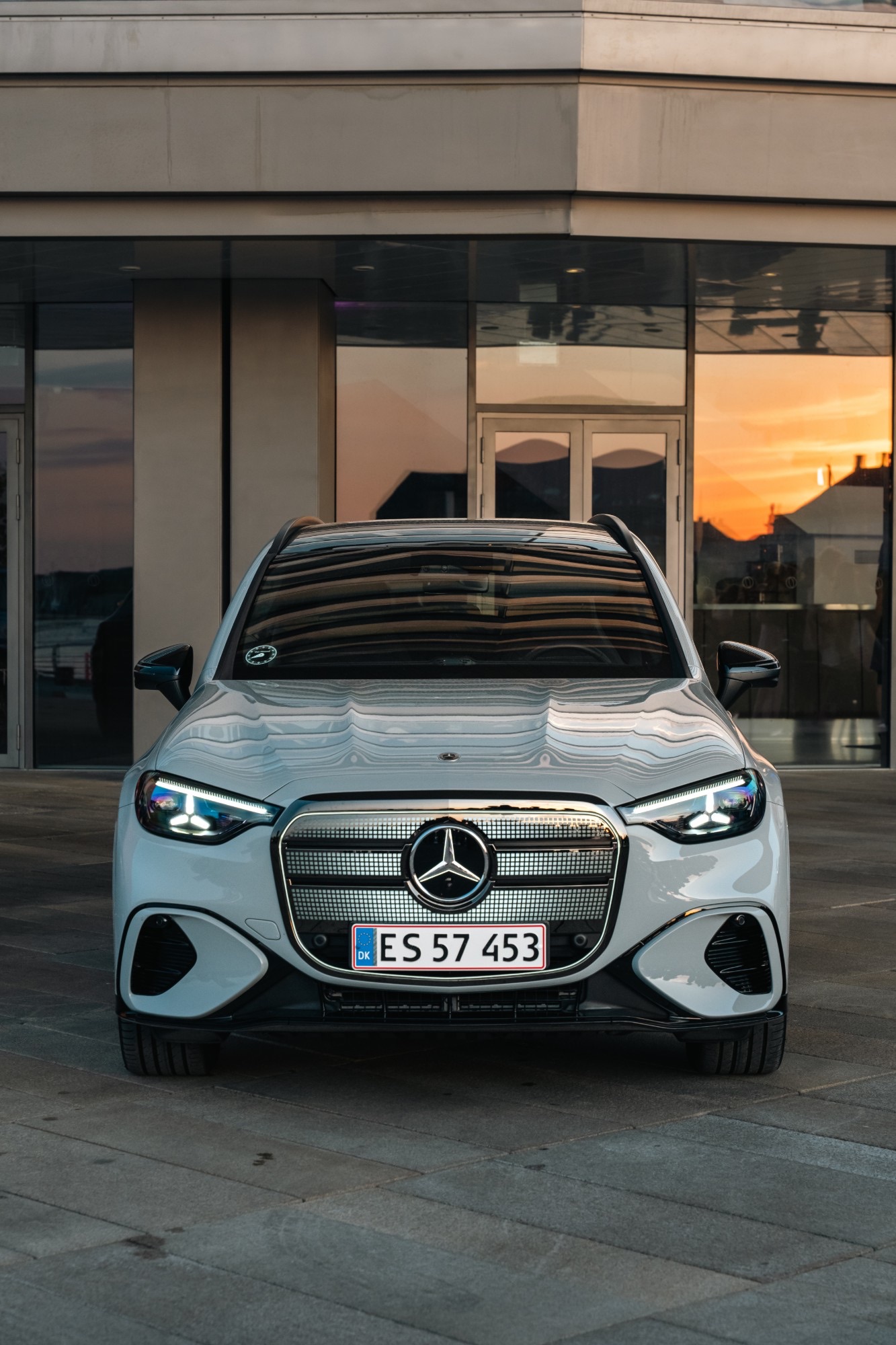 A silver Mercedes-Benz outside a glass building at sunset